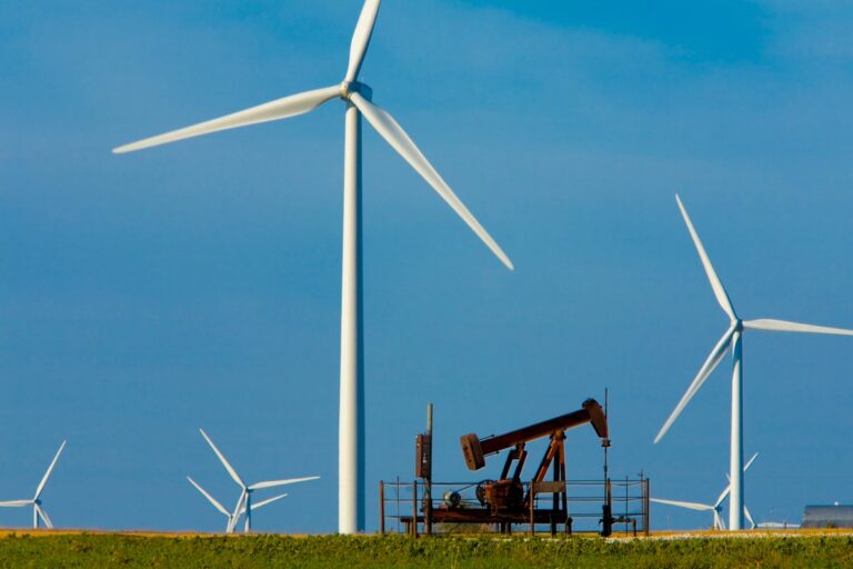 Blades of Wind Turbines surround Oil Well pumping unit inAgricultural Field