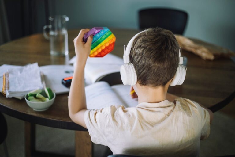 Rear view of boy listening to music and playing with push pop toy while doing homework