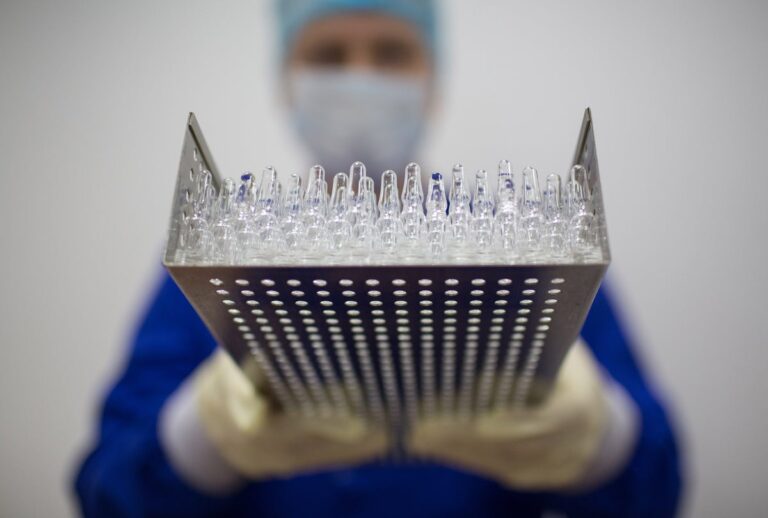 A lab worker holds a tray containing unlabeled vaccine bottles
